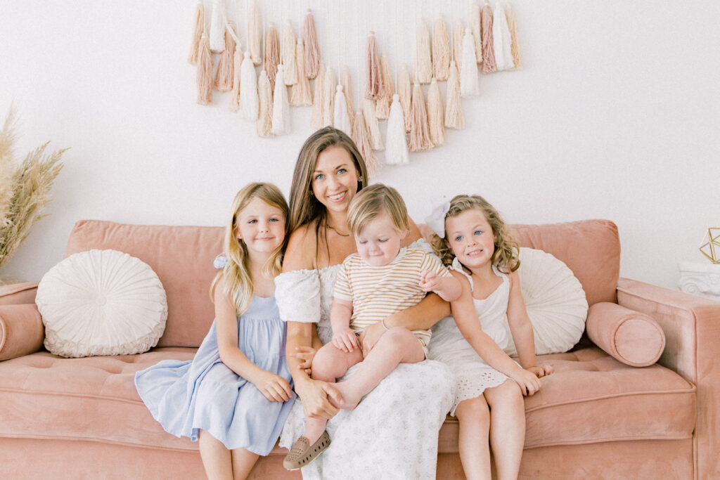 A mother, her two daughters, and her son sitting on a pink couch for Fort Worth family photos by Cynthia Knapp Photography